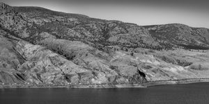 Kanadische Panoramalandschaft mit einem Güterzug zwischen dunklem Flusswasser und schroffen Hügeln