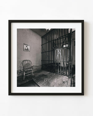 An iron cell door and worn wooden chair inside Gardner’s old jail in Illinois, photographed in black and white