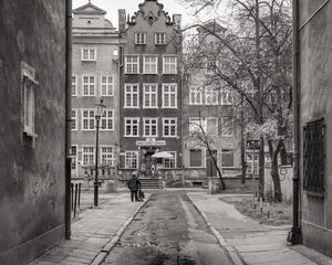 Weathered walls frame a quiet Gdańsk street with a pedestrian and ornate buildings