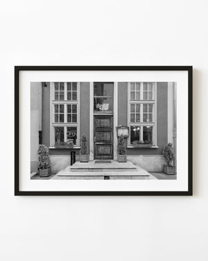 A wooden restaurant door stands between tall windows in a black and white Gdańsk photograph