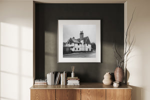 Ingelijste zwart-witfoto van een huis aan de muur boven een houten kast met decoratieve spullen.