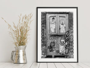 Black and white street photography captures pasted artwork within a brick window surround
