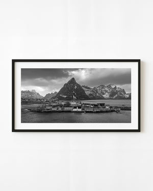 Hamnøy waterfront cabins stand beneath snow-streaked Lofoten peaks in black and white