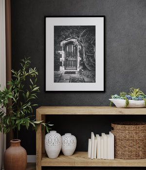 A vertical monochrome photograph captures an old doorway entwined with climbing vines