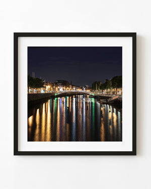 Ha’penny Bridge crosses Dublin’s River Liffey before dawn with colourful lights reflected on the water.
