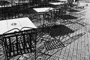 Wrought-iron cafe chairs create long shadows on brick paving in Havana’s Plaza Vieja.
