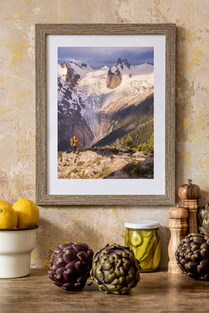 A hiker raises a camera toward a glacier flowing between steep mountain walls.