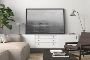 A humpback whale raises its broad tail against a pale, hazy horizon in monochrome.