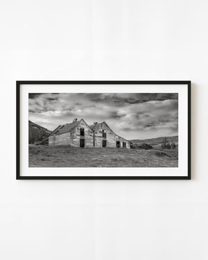 Abandoned double-gabled building in Iceland beneath a dramatic clouded sky, photographed in black and white.