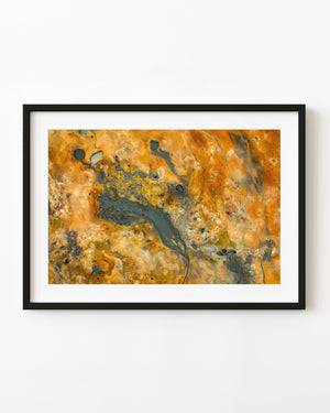 Luftaufnahme eines grauen geothermischen Schlammbeckens inmitten von orange und gelb mit Mineralien gefärbtem Boden in Island.