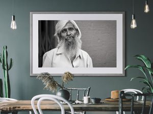 A man’s long white beard and softly smiling expression against a plain textured wall in India.
