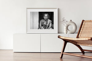 Monochrome doorway portrait of an older woman with a thoughtful gaze and softly lit face.