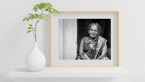 An older woman sits in a shaded doorway in India, her patterned saree illuminated by soft light.