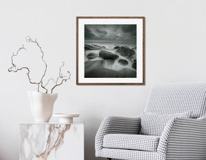 Waves sweep between rounded coastal rocks beneath an overcast sky.