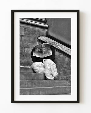Man reading a newspaper on stone steps in Manhattan in black and white