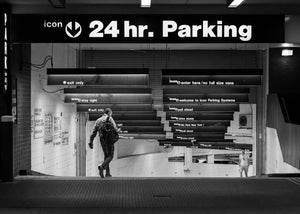 Two men on a New York parking garage ramp beneath rows of illuminated signs