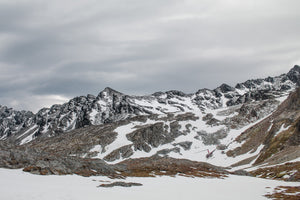 Verschneite Martial Mountains und ein entfernter Hubschrauber unter einem bewölkten Himmel