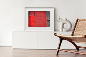 Porte métallique rouge et rideau horizontal contrastant avec des briques grises.