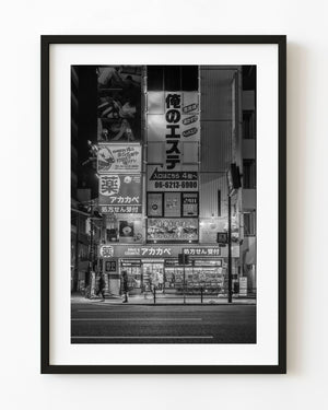 Illuminated Osaka storefront beneath stacked Japanese signs at night, black and white