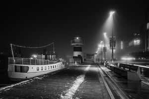 Schwarz-weißer Pier von Aker Brygge mit einem Boot und leuchtenden Straßenlaternen