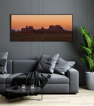 Monument Valley at sunrise with dark red cliffs and a pale peach sky
