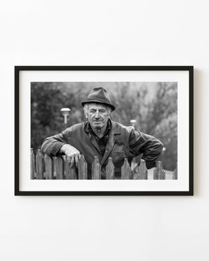 black and white portrait of rural Romanian farmer leaning on wooden fence