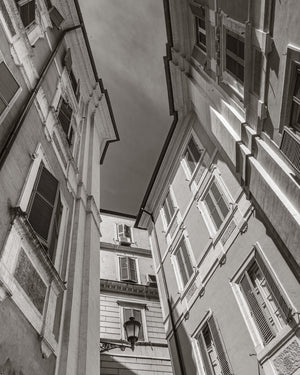 Black and white photograph looking upward between historic buildings in Rome