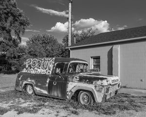 Black and white photograph of a worn vintage truck with painted side lettering