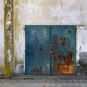 Fotografía en color de puertas azules corroídas rodeadas de yeso pálido manchado