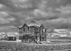 Two-storey wooden farmhouse standing in open prairie grass