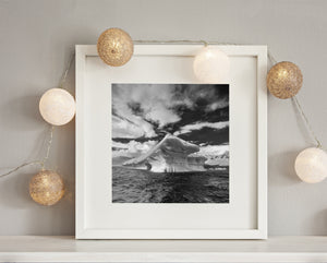 Monochrome polare Meereslandschaft mit einem verwitterten Eisberg unter dramatischen Wolken