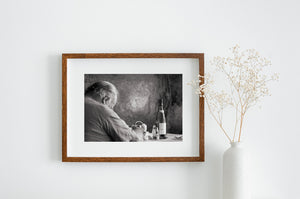 Grey-haired man leaning forward at a table against a textured wall