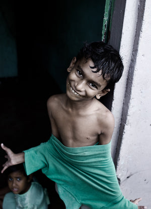 Young boy smiling beside a white doorway with a green shirt around his waist