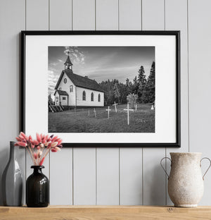 White clapboard church and grave markers framed by northern woodland.