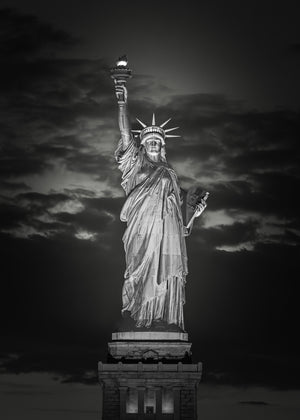 Freiheitsstatue leuchtet unter einem dramatischen Nachthimmel.