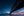 The underside of Sydney Harbour Bridge leads toward city lights beneath a deep blue sky.