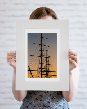 Fine ropes form a web around tall ship masts in evening light.