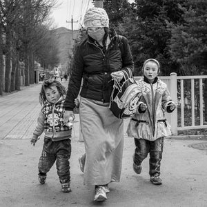 A woman in a knitted hat and face covering walks between two children.