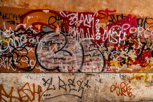 Colourful spray-painted tags on peeling orange plaster in Tivoli