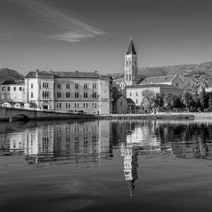 Black and white Trogir architecture with a tall bell tower mirrored in calm water.
