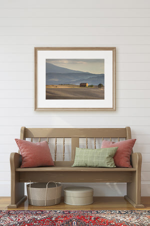 Quiet Tuscan landscape with a small farmhouse and softly layered mountain slopes.