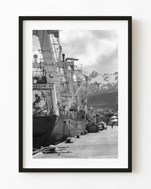 Commercial ship moored beneath snowy mountains in Ushuaia, Argentina, in black and white