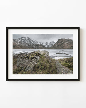 Ice-covered Vikvatnet Lake beneath snowy Norwegian mountains with mossy rocks in front