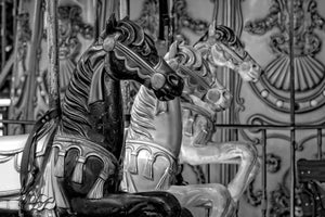 明るい色の馬と華やかな遊園地パネルの前に立つ暗いメリーゴーランド馬