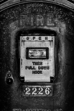Weathered cast-metal fire alarm with raised lettering and a worn pull-down instruction panel