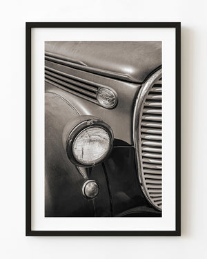 Vintage Ford pickup headlight, oval emblem and curved grille in warm sepia tones