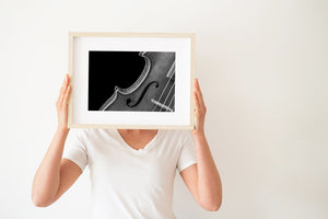 Curving edge of a violin beside its strings in monochrome.