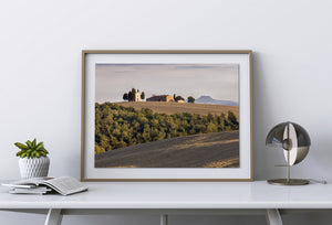 Chapel and farmhouse on a ridge above wooded Tuscan hills.
