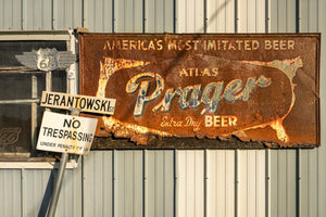 Rostiges Atlas-Prager-Bierschild neben Straßenschildern