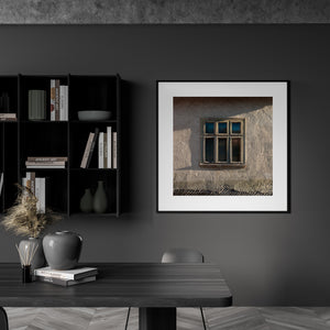 Square photograph of a weathered farmhouse window beneath diagonal shadows